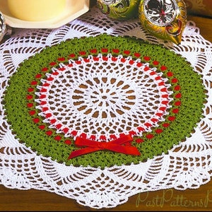 May include: White crochet doily with a green and red wreath design in the center. The wreath has a red bow in the center.