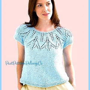May include: Light blue knit top with a decorative openwork design around the neckline and sleeves. The short-sleeved shirt is a solid color with a slightly textured appearance. The text "PastPatternPaloozaCo" is visible on the shirt.