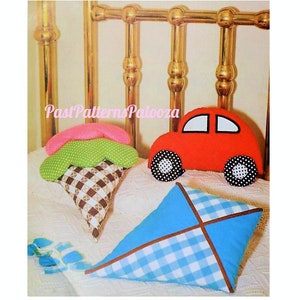May include: Three plush toys on a bed: a red car with black polka dot wheels, a green and pink ice cream cone, and a blue and white checked kite.