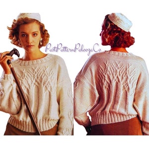 May include: Cream-colored, oversized knit sweater with a crew neck and intricate leaf-like cable knit design on the front and back. The sweater has a ribbed hem and cuffs. The image also shows a matching hat and a cane with a horse head handle.