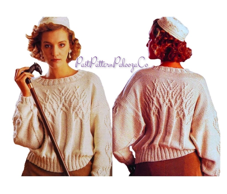 May include: Cream-colored, oversized knit sweater with a crew neck and intricate leaf-like cable knit design on the front and back. The sweater has a ribbed hem and cuffs. The image also shows a matching hat and a cane with a horse head handle.