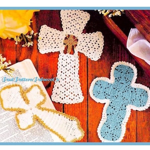 May include: Three crocheted crosses, one white, one blue, and one white with gold trim. The crosses are on a wooden surface with a book and flowers.