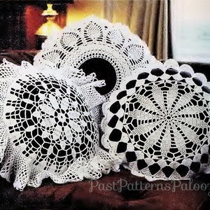 May include: Three white crocheted doilies, two are round and one is a square with rounded corners. The doilies are arranged on a dark brown surface.