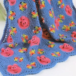 May include: A blue crocheted baby blanket featuring a pink pig design and colourful flower accents.
