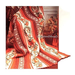 May include: A vintage crochet blanket with a floral pattern in shades of orange, white, and brown. The blanket features a striped design with alternating patterns, including cable knit and diamond shapes. The blanket is draped over a chair.