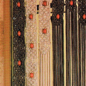 May include: A macrame curtain with three panels, each with a different pattern. The panels are made of brown, white and beige cords and have red wooden beads woven into the design.