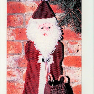 K&ouml;nnte beinhalten: Geh&auml;kelte Weihnachtsstrumpf mit einem rot-wei&szlig;en Anzug, wei&szlig;em Bart und einem braunen Sack mit Zuckerstangen. Der Strumpf h&auml;ngt an einer Backsteinwand.