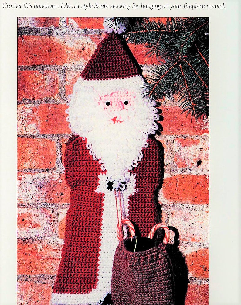 K&ouml;nnte beinhalten: Geh&auml;kelte Weihnachtsstrumpf mit einem rot-wei&szlig;en Anzug, wei&szlig;em Bart und einem braunen Sack mit Zuckerstangen. Der Strumpf h&auml;ngt an einer Backsteinwand.
