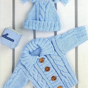 May include: A light blue knitted baby cardigan with a cable knit pattern and wooden buttons. The cardigan has a collar and long sleeves. A matching light blue knitted hat with two pom-poms is also included.