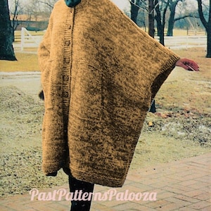 May include: A brown knitted hooded cape with a button closure. The cape is worn by a person standing on a brick walkway.