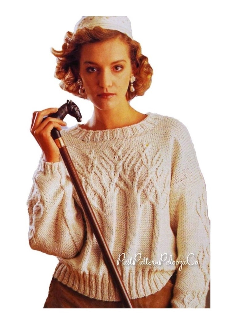 May include: Cream-colored knitted sweater with a tree-like pattern on the front. The sweater has a round neckline and ribbed cuffs and hem. A dark brown walking stick with a horse head handle is held in the hand.