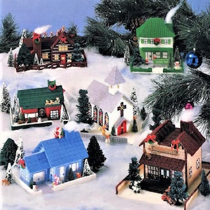 May include: A set of six plastic canvas Christmas village houses. The houses are decorated with red, green, and white paint and have various details, including a church with stained glass windows, a house with a Santa Claus on the roof, and a house with a reindeer on the roof.