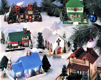 May include: A set of six plastic canvas Christmas village houses. The houses are decorated with red, green, and white paint and have various details, including a church with stained glass windows, a house with a Santa Claus on the roof, and a house with a reindeer on the roof.