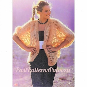 May include: A light brown knitted cardigan with a loose, open-weave design. The cardigan has a shawl collar and long sleeves. The model is wearing the cardigan over a black dress.