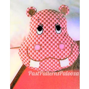 May include: Pink and white gingham fabric hippopotamus pillow with embroidered eyes, nose, and teeth. The pillow is a handmade craft item.