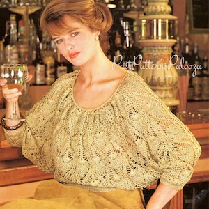 Puede incluir: Un top de crochet beige claro con cuello redondo y mangas tres cuartos. El top presenta un delicado patrón calado y un diseño ligeramente fruncido en el escote. La imagen está ambientada en un bar con el texto "Past Patterns Palooza".