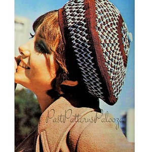 Peut inclure: Une femme portant un béret crocheté brun, blanc et bleu avec un bouton sur le dessus. Le béret a un motif géométrique. La femme porte un manteau marron.