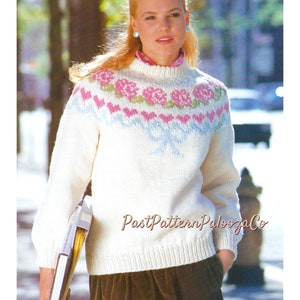 May include: A white knitted sweater with a pink, blue, and green floral pattern around the neckline. The sweater has a crew neck and long sleeves.