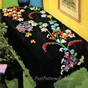 May include: A black crochet throw blanket with a floral design in shades of red, orange, yellow, green, blue, and purple. The blanket has fringe on the bottom edge.