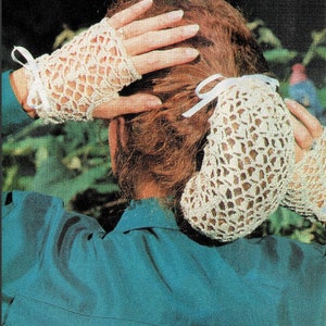 Könnte beinhalten: Ein Paar weiße, fingerlose Handschuhe aus Häkelarbeit mit weißen Schleifenbändern. Die Handschuhe sind mit einem zarten Lochmuster gearbeitet.
