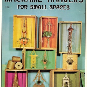 Könnte beinhalten: Ein Buchcover mit dem Titel "Macrame' Hangers for Small Spaces" und der Nummer H-228. Das Cover zeigt eine Collage aus Makramee-Pflanzenhängern in verschiedenen Farben und Stilen, die auf Holzregalen ausgestellt sind.