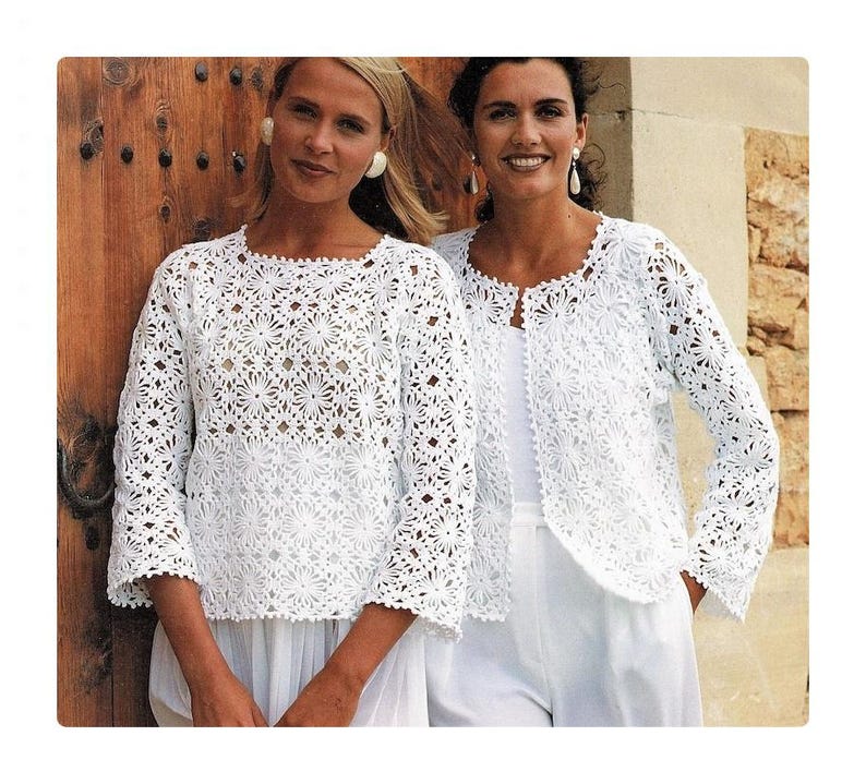 May include: Two women wearing white crocheted jackets with a floral pattern. The jackets are open in the front and have long sleeves. The women are standing in front of a wooden door.