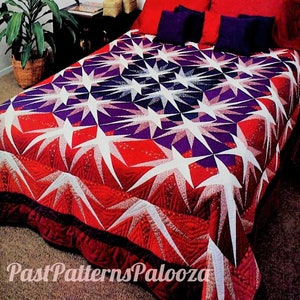 May include: A red, white, and purple quilt with a starburst pattern. The quilt is on a bed with red and purple pillows.