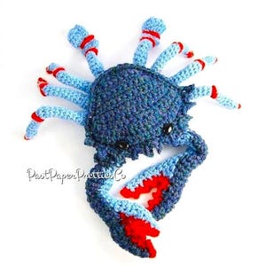 May include: A crocheted blue crab with red accents. The crab has a textured body and large claws.