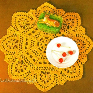 May include: A yellow crocheted doily with a decorative pattern. A small white plate with red cherries on top sits on the doily. A small green box with a painted animal design is also on the doily.