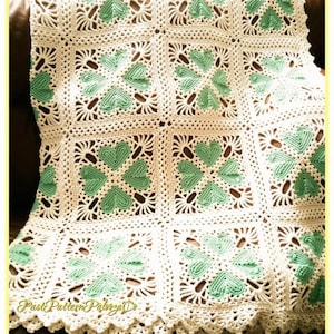 May include: A handmade crochet blanket featuring a repeating square motif pattern. Each square contains four mint green heart-shaped elements arranged in a clover design, surrounded by white yarn. The blanket has a decorative scalloped edge.