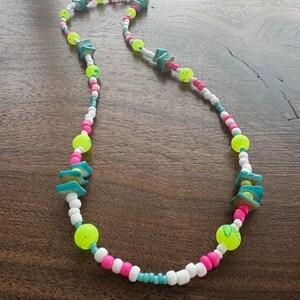 May include: A colorful beaded necklace with turquoise, white, pink, and neon yellow beads. The necklace features larger turquoise beads in the shape of a triangle.