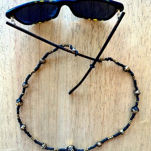 May include: A black and gold beaded glasses chain with a tortoiseshell frame sunglasses.