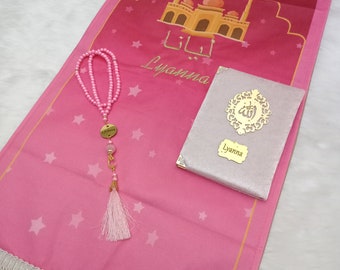 Peut inclure: Tapis de prière rose avec une frange blanche, un motif de mosquée doré et le nom "Lyanna" écrit en caractères arabes. Le tapis comprend également un collier de prière en perles roses avec un pompon doré et un petit livre blanc avec le nom "Lyanna" sur la couverture.