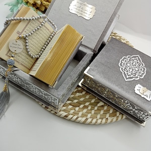 May include: A gray velvet box set with intricate silver designs. The box contains a Quran, prayer beads, and a small silver charm with the text "Keep me in your Duas".