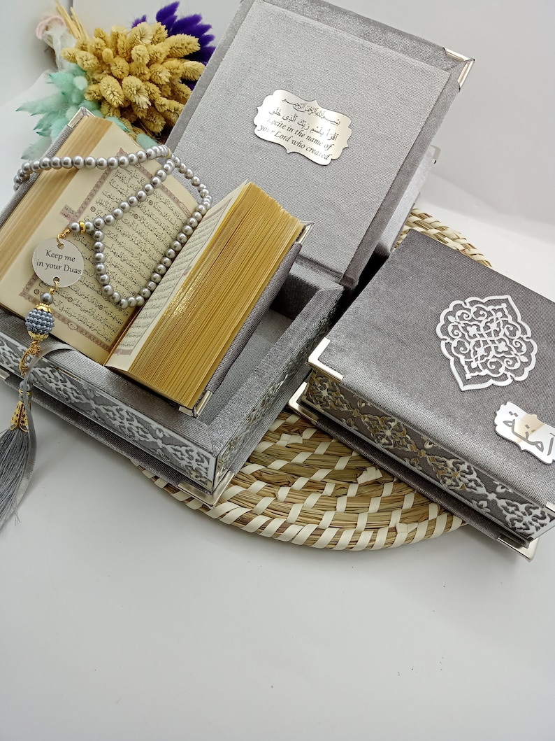 May include: A gray velvet box set with intricate silver designs. The box contains a Quran, prayer beads, and a small silver charm with the text "Keep me in your Duas".