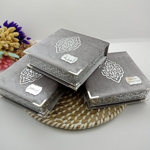 May include: Three gray velvet boxes with silver trim and intricate designs. The boxes have different inscriptions: "Keep me in your Duas", "Yousef", and "أمنه".