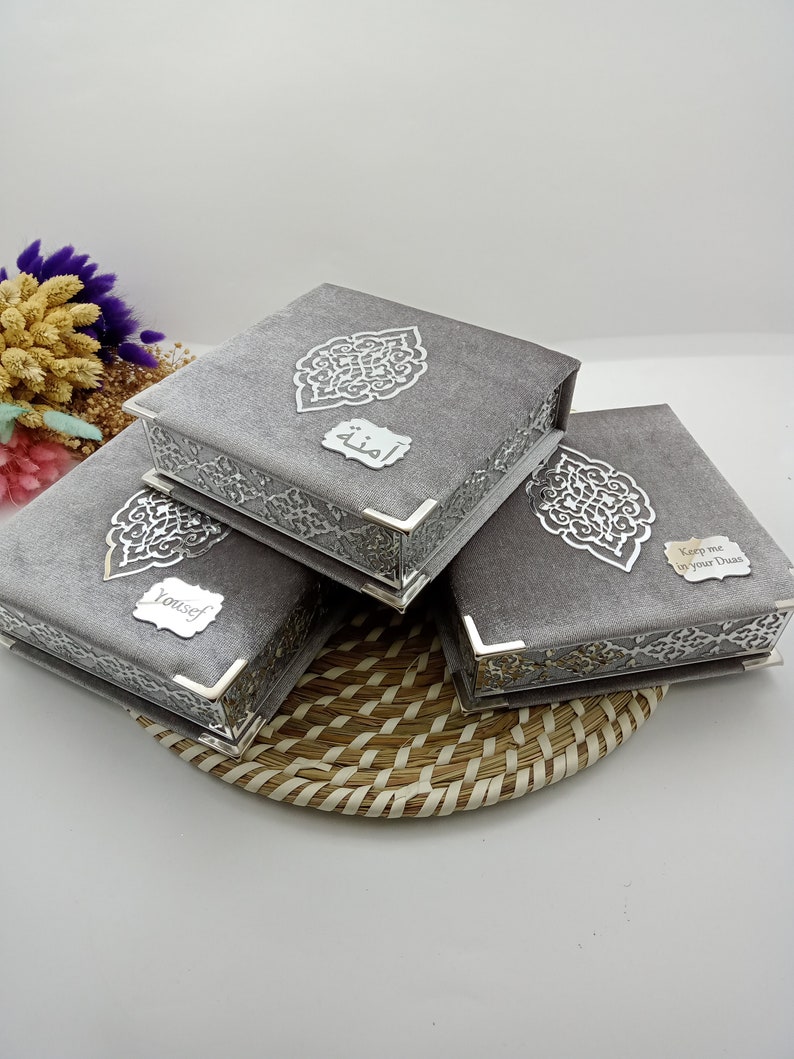 May include: Three gray velvet boxes with silver trim and intricate designs. The boxes have different inscriptions: "Keep me in your Duas", "Yousef", and "أمنه".
