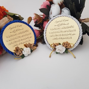 May include: Two circular gold plaques featuring Arabic calligraphy, edged with blue and silver rope. Each plaque is decorated with white, gold, and brown floral arrangements. The text "Ayat'ul Kursi" is displayed on each plaque.