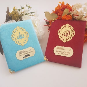 Pode incluir: Dois livros de veludo, um turquesa e outro vermelho, com detalhes dourados. Cada livro apresenta um design de filigrana dourada e uma placa dourada com escrita &aacute;rabe e texto em ingl&ecirc;s. O livro turquesa diz "Sara's Graduation".