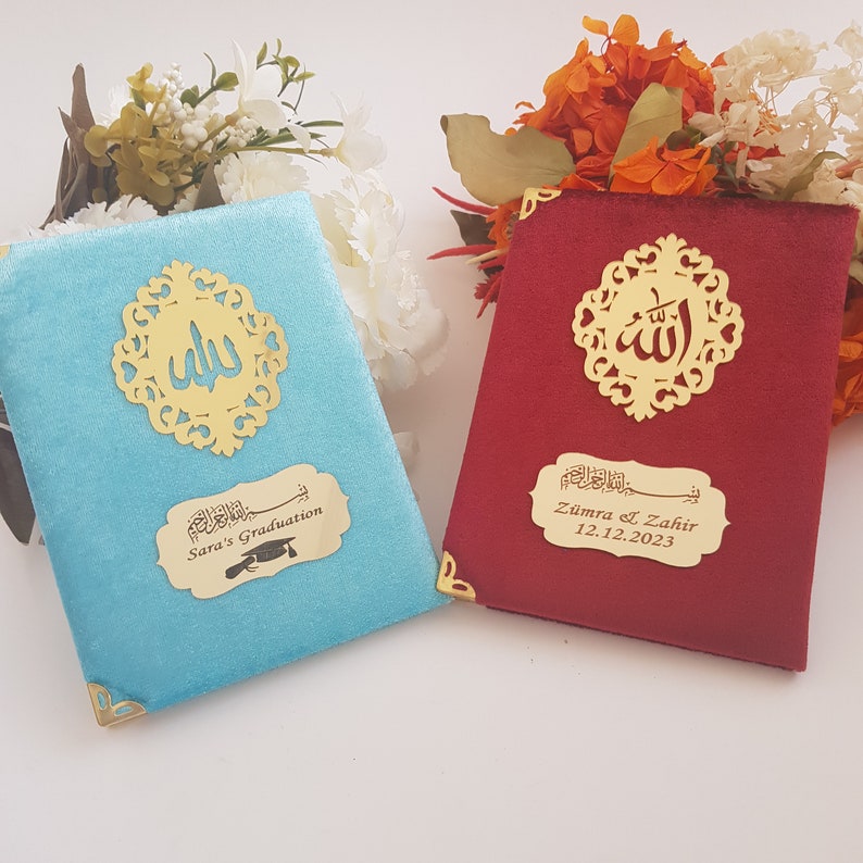 Pode incluir: Dois livros de veludo, um turquesa e outro vermelho, com detalhes dourados. Cada livro apresenta um design de filigrana dourada e uma placa dourada com escrita &aacute;rabe e texto em ingl&ecirc;s. O livro turquesa diz "Sara's Graduation".