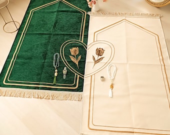 May include: Two prayer rugs with gold trim and fringe. One rug is green with a gold tulip design, the other is cream with a gold tulip design. Both rugs have prayer beads and a small gold charm.