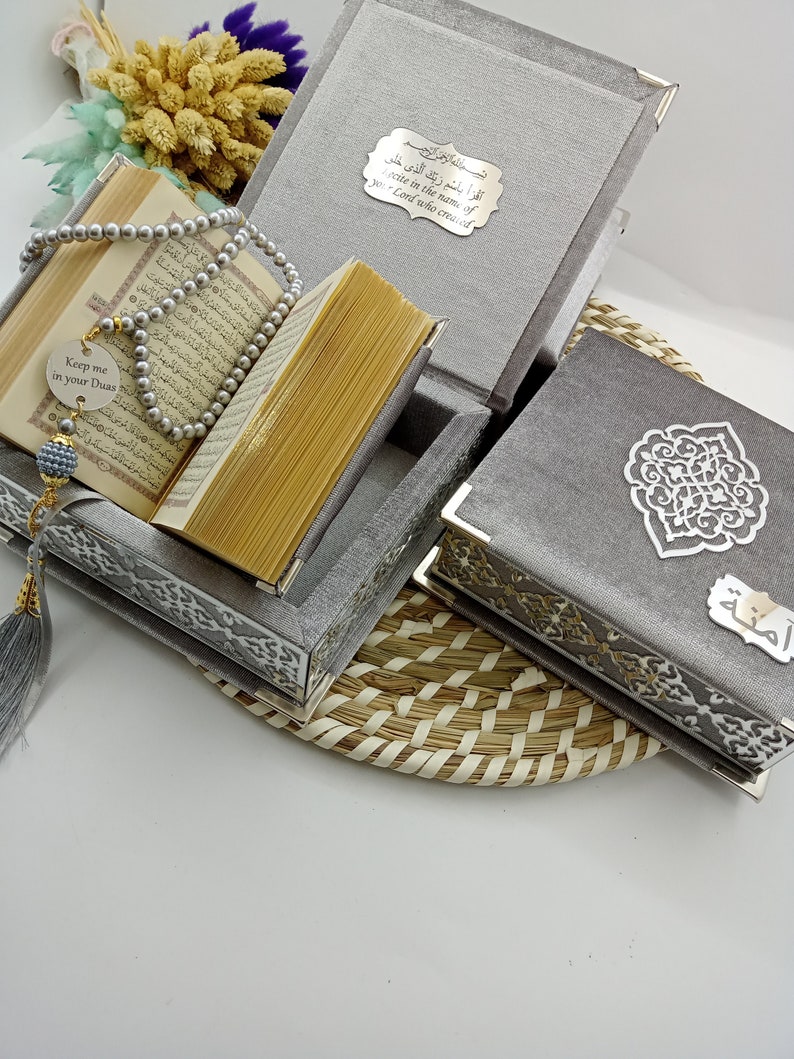 May include: A gray velvet box set with intricate silver designs. The box contains a Quran, prayer beads, and a small silver charm with the text "Keep me in your Duas".