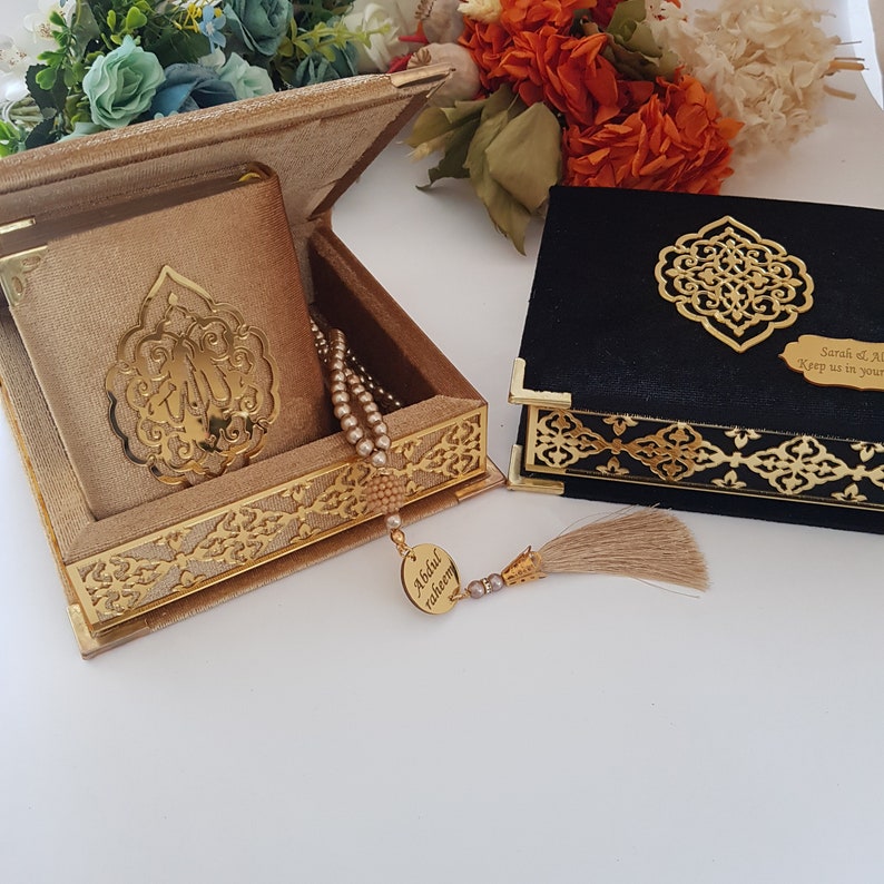 May include: A gold velvet box with a gold-colored metal design and a gold-colored tassel. The box contains a small book with a gold-colored design and a string of beads. The box is sitting on a white surface. The text on the box reads "Abdul raheem".