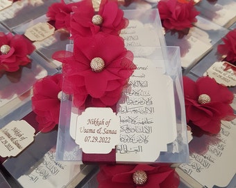 May include: Red and gold decorative boxes with a floral design and the text "Nikkah of Usama & Sanaa 07.29.2022" on the front. The boxes are filled with small gifts and are perfect for a wedding or other special occasion.