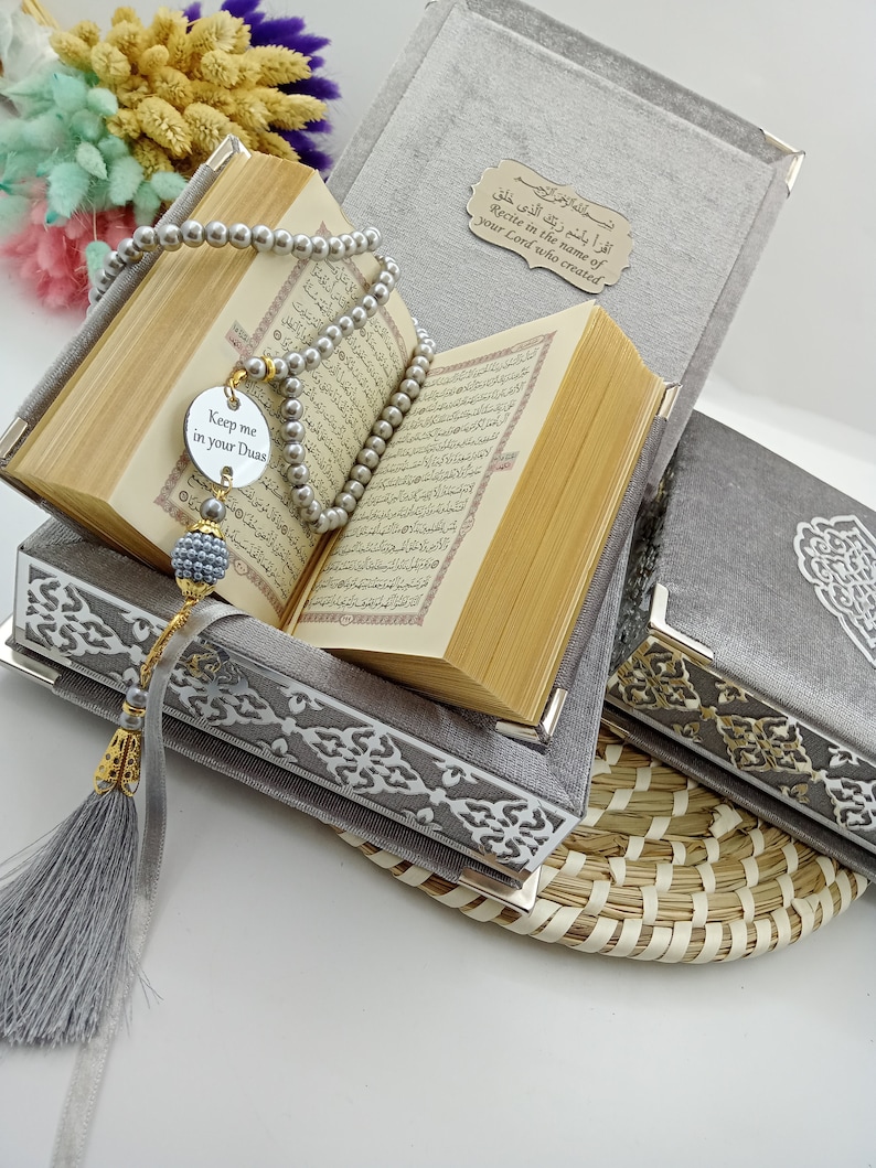 May include: A gray velvet box with a Quran inside, a silver prayer bead necklace, and a silver charm that says "Keep me in your Duas". The box has a gold inscription that reads "Recite in the name of your Lord who created".