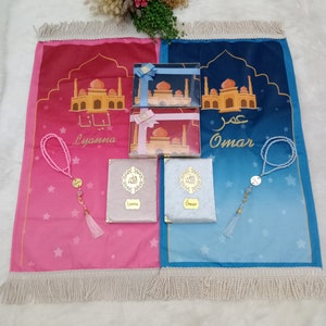May include: Two prayer mats in pink and blue featuring mosque illustrations and the names Lyanna and Omar. Includes two matching gift boxes with ribbons, two velvet-covered books with gold calligraphy, and two sets of beaded prayer beads with tassels.