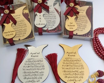 May include: Two silver and gold decorative ornaments shaped like pomegranates with red tassels. The ornaments have Arabic text on them and the words "Ayat'ul Kursi" are visible. The ornaments are in front of three gift boxes with red bows and red and gold beads.