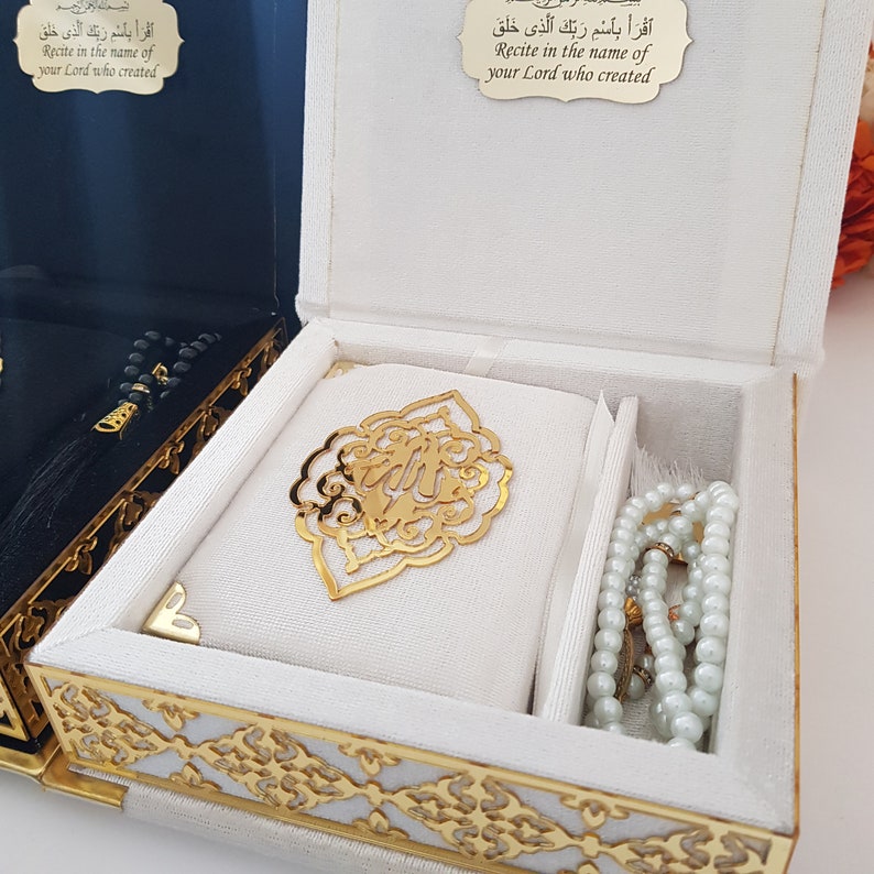 May include: White box with gold trim and intricate designs. Inside the box is a white prayer rug with a gold metal design, and a white prayer bead necklace.