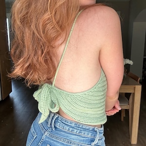 Puede incluir: Un top de crochet verde claro con un detalle de nudo en la espalda. El top se lleva con jeans azules.