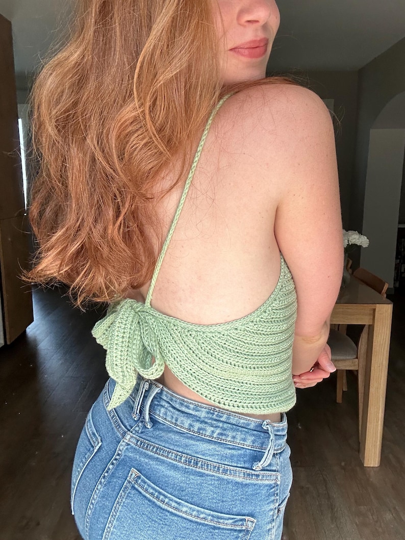 Puede incluir: Un top de crochet verde claro con un detalle de nudo en la espalda. El top se lleva con jeans azules.
